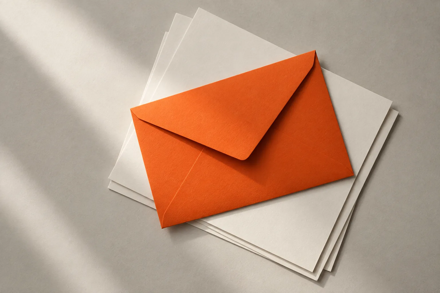 An orange envelope on sheets of white paper in soft daylight: a personal message.